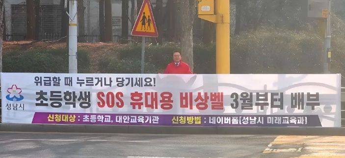 황금석 성남시의원이 초등학교 인근에 설치된 ‘초등학생 SOS 휴대용 비상벨’ 신청 안내 현수막 앞에 서 있다